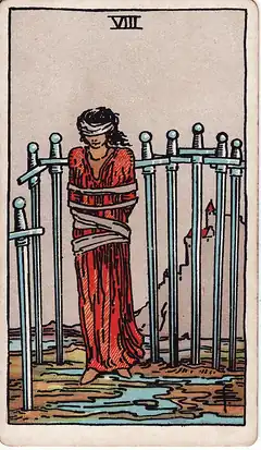 Eight of Swords. A woman stands bound and blindfolded among eight swords set in the mud, the ropes loose, a castle on the hill behind.
