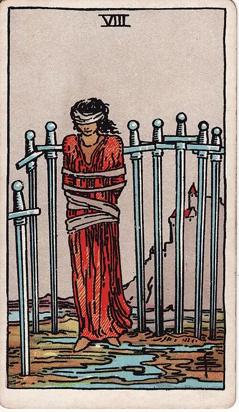 Eight of Swords. A woman stands bound and blindfolded among eight swords set in the mud, the ropes loose, a castle on the hill behind.