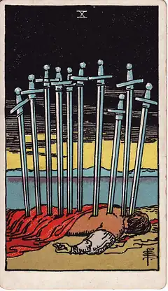 Ten of Swords. A man lies face down on the shore with ten swords in his back, under a black sky with the first light on the horizon.