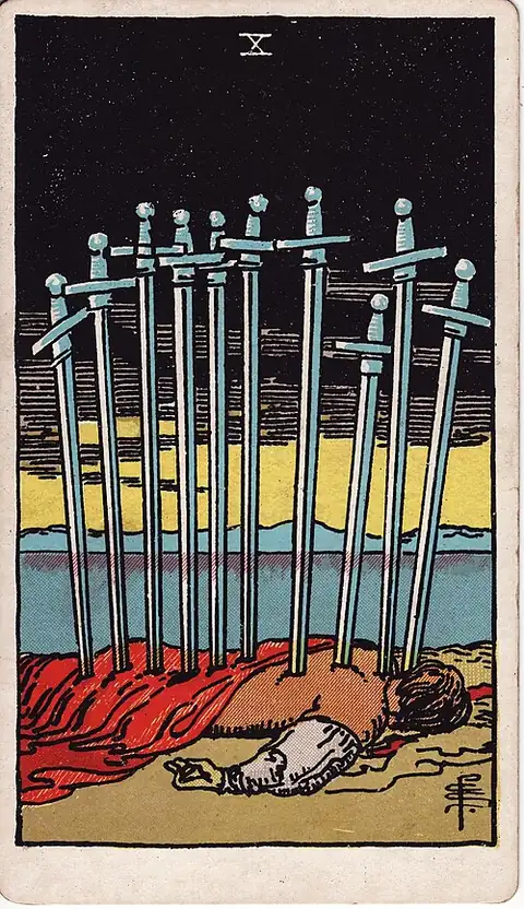 Ten of Swords. A man lies face down on the shore with ten swords in his back, under a black sky with the first light on the horizon.
