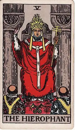 The Hierophant. A robed priest between two stone pillars raises a hand in blessing over two tonsured monks, with crossed keys on the floor.