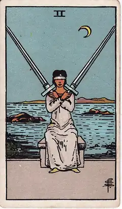 Two of Swords. A blindfolded woman sits with two swords crossed over her chest, a rocky sea and a crescent moon behind.