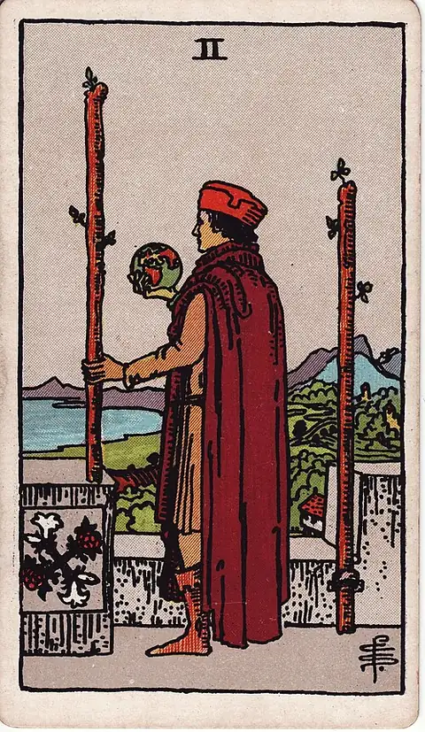 Two of Wands. A man in a castle courtyard holds a globe in one hand and a staff in the other, looking out over the sea past a second staff fixed to the wall.